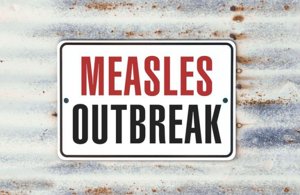 A road sign with the words "Measles Outbreak" in red and black against a wavy white and rusted steel background